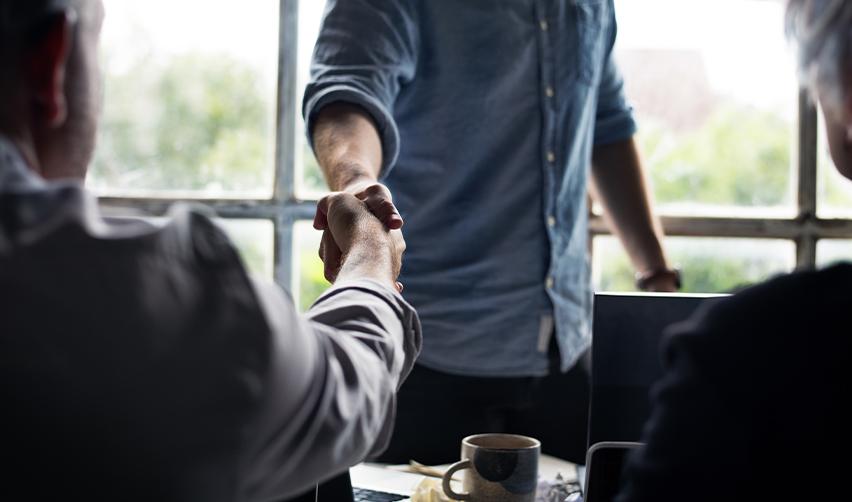Close-up of a handshake between professionals in an office setting, representing trusted EB5 guidance and investor support services by EB5AN.