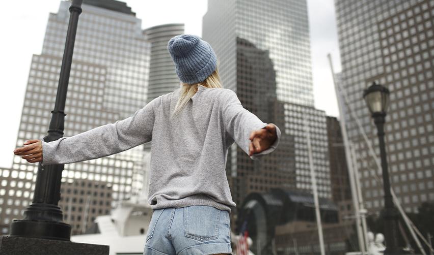 A woman stretches her arms wide while standing in a modern U.S. cityscape, representing the freedom and new beginnings EB5 investors experience while living in the U.S.