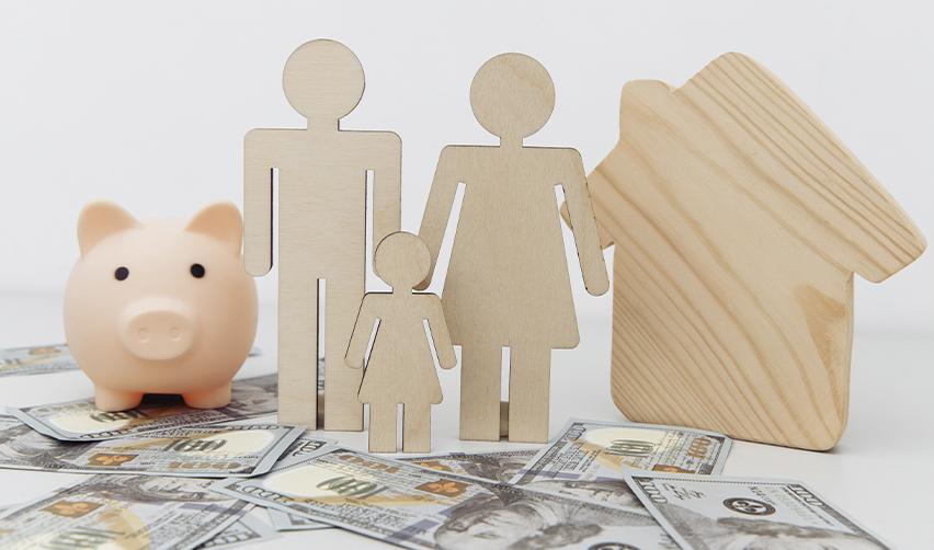 Wooden cutouts of a family and a house on U.S. dollars with a piggy bank, symbolizing financial security and long-term family investment through the EB5 program.