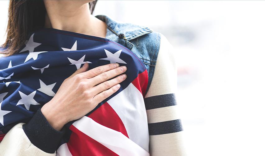 A woman holding the American flag with her hand over her heart, symbolizing patriotic values and the importance of maintaining one’s visa status under evolving U.S. immigration rules like the new catch and revoke policy.