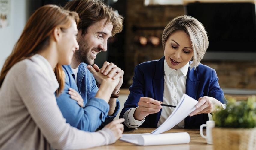 Financial advisor explaining investment documents to a smiling couple, representing EB5 investors reviewing project terms and repayment timelines.