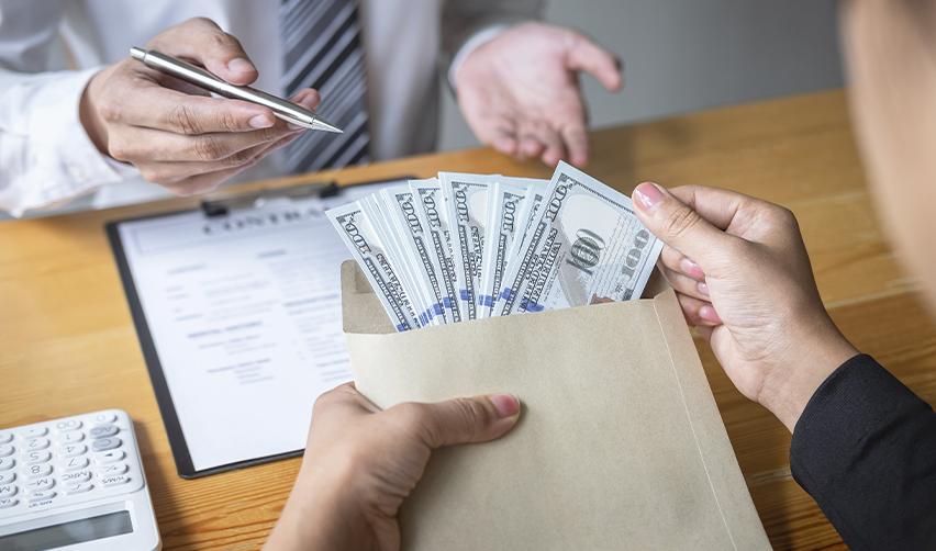 Person handing over an envelope filled with U.S. dollar bills during a business meeting, illustrating private loan funding for an EB5 investment.