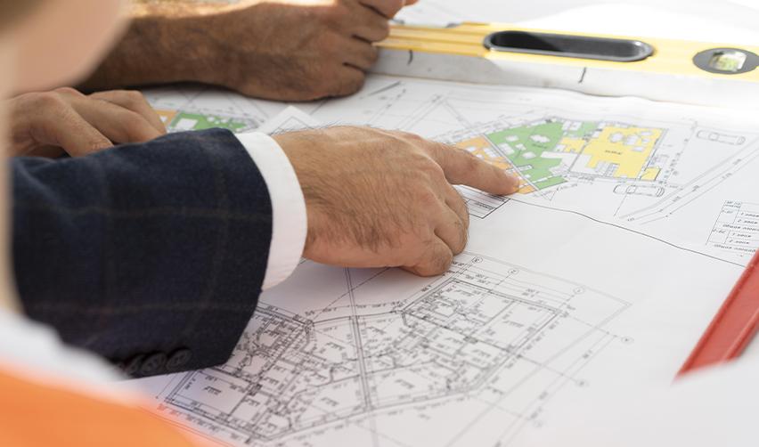 Close-up of an architect’s hand pointing at a colorful building plan, representing detailed project planning for EB5-eligible residential construction.