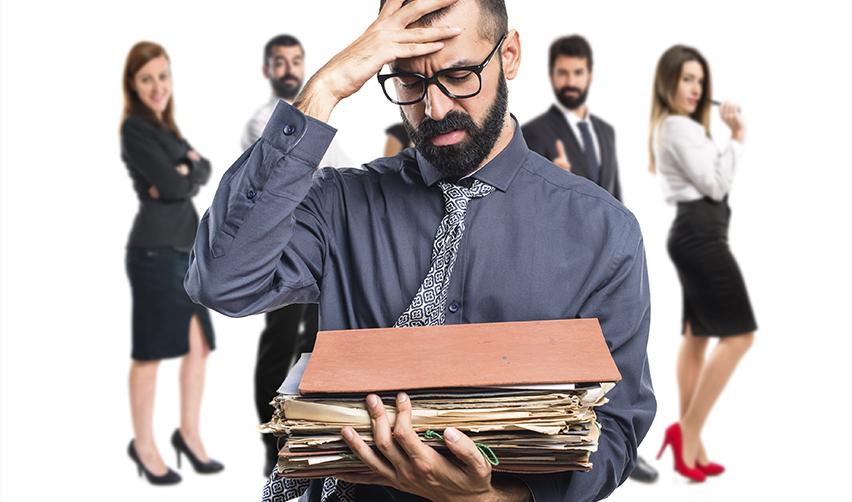 Frustrated office worker holding a large stack of files, symbolizing the challenges, uncertainty, and strict requirements of the H1B visa process compared to EB5 stability.