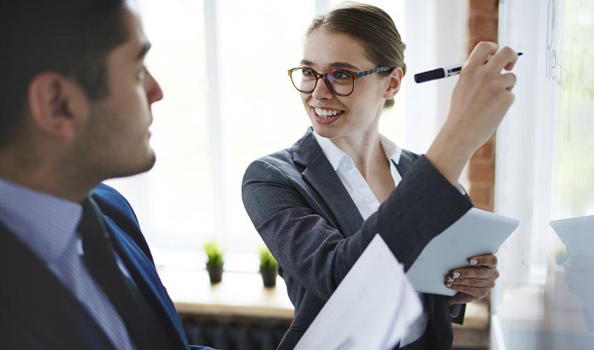 Businesswoman explaining financial compliance requirements to a colleague using a whiteboard, highlighting USCIS source of funds rules for EB5 loans.