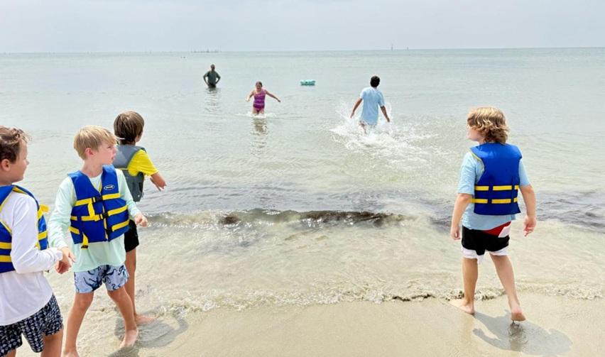 Children in life jackets enjoying summer activities on Bay Creek’s shoreline, highlighting family-friendly amenities that strengthen community appeal.
