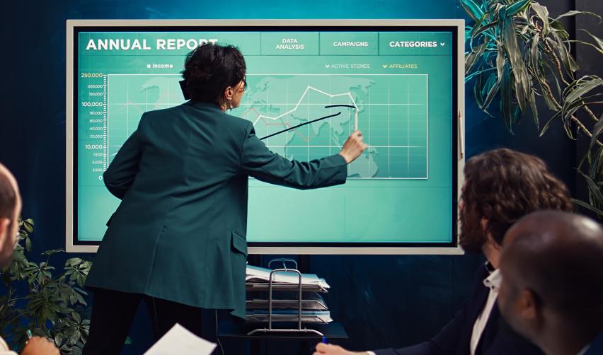 A business professional presenting an annual report with charts and graphs to colleagues, representing EB5 job creation and financial tracking updates for investors.