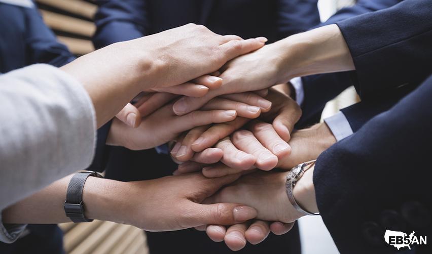 The EB5AN logo next to hands stacked together in unity, representing the teamwork of regional centers, legal experts, economists, and fund administrators working toward successful EB5 outcomes.