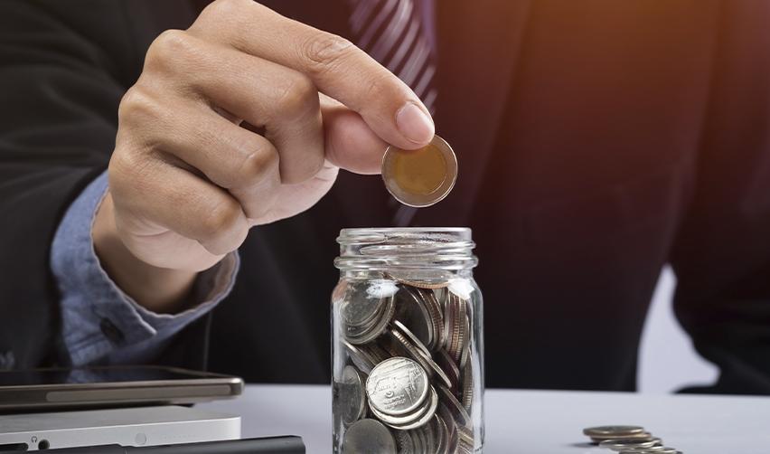 Businessperson placing a coin into a jar of savings, representing EB5 investors documenting personal savings as part of their source of funds.