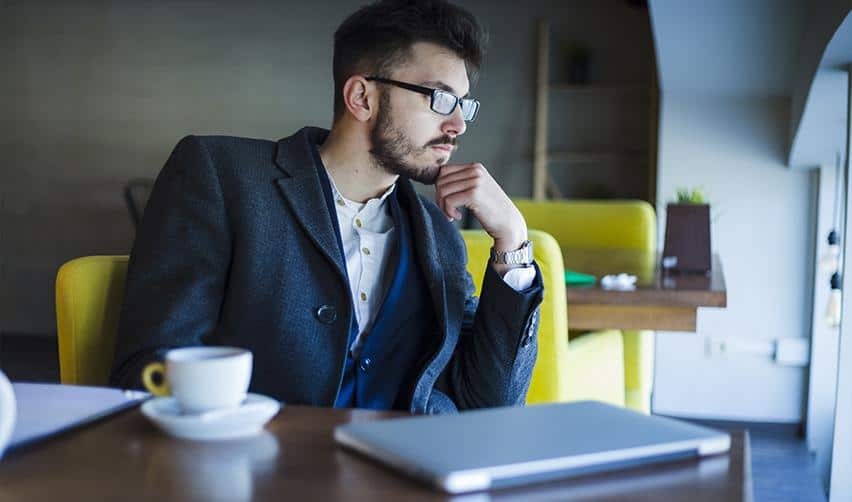 A thoughtful man sitting with coffee and a laptop, reflecting on EB5 investment options and immigration planning.