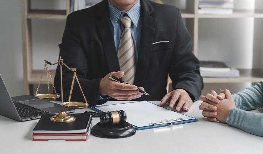Attorney consulting with a client at a desk with legal scales and gavel, representing the importance of working with EB5 immigration attorneys for source of funds.