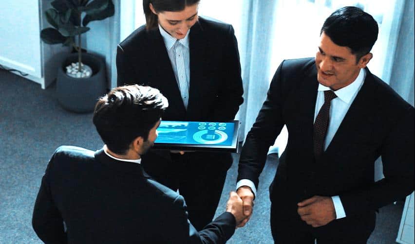 EB5 investors and EB5AN regional center representatives shaking hands, with someone holding a tablet, showing the strong technological support EB5 investors receive.