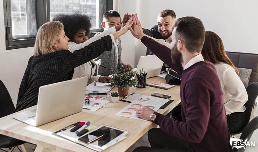 EB5AN logo next to a diverse group of EB5 professionals celebrating a milestone with high-fives at the office, reflecting teamwork, integrity, and proven success in EB5 investments.