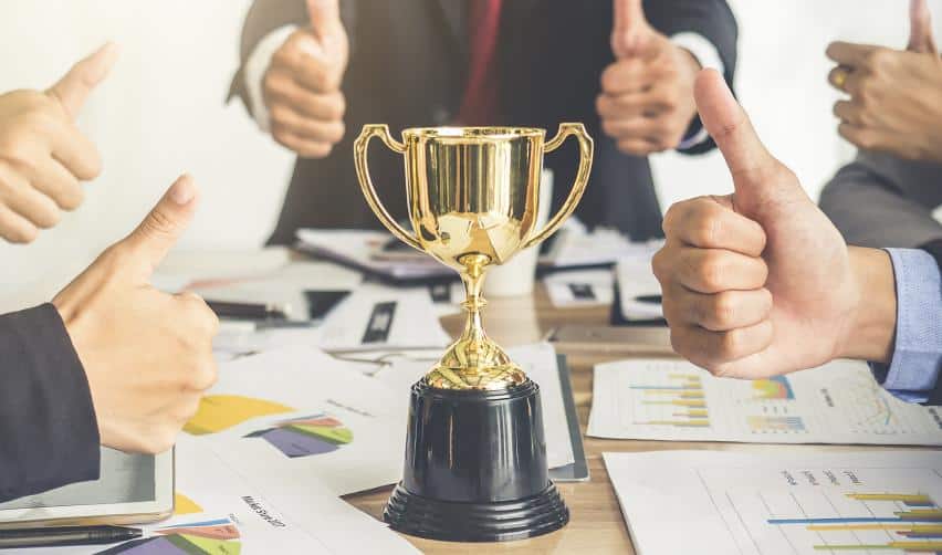 A trophy surrounded by team members giving thumbs up, symbolizing successful EB5 project performance, investor confidence, and strong compliance record.