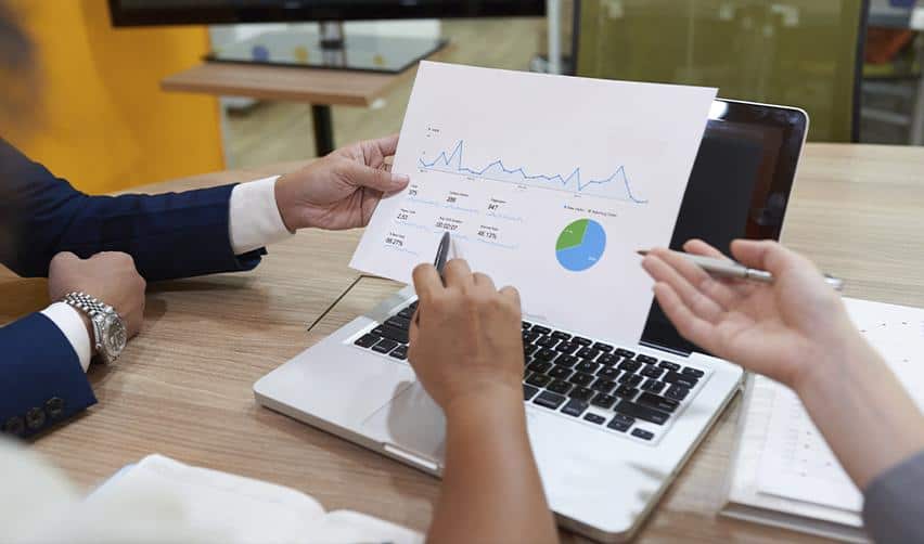 Two professionals reviewing charts and data on a laptop during a meeting, illustrating EB5 investors analyzing case progress, processing trends, and immigration timelines.