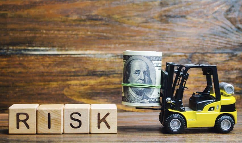 A forklift lifting rolled U.S. dollar bills next to blocks spelling risk, symbolizing capital risk management, secured loan structures, and downside protection in EB5 investment projects.