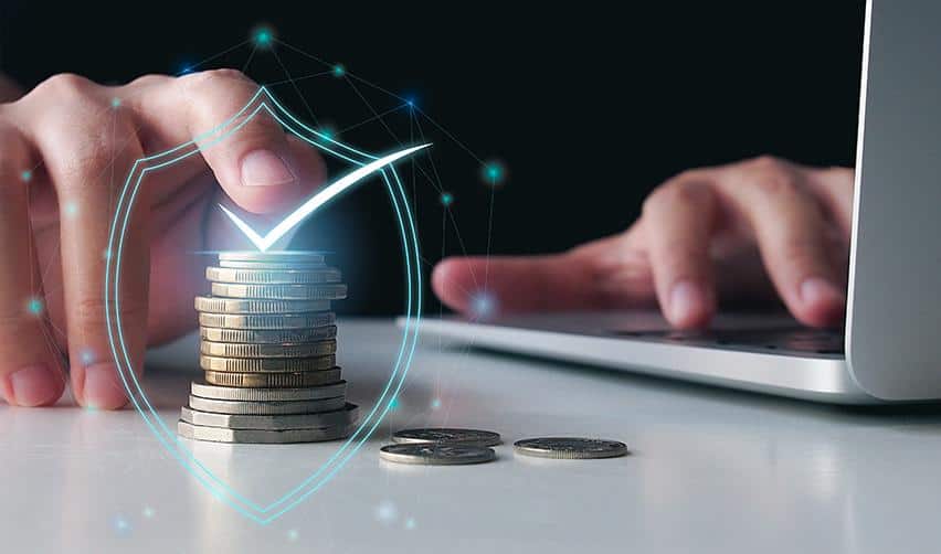 A stack of coins protected by a digital shield icon next to a laptop, representing capital security, risk mitigation, and senior EB5 loan structures that prioritize investor repayment.