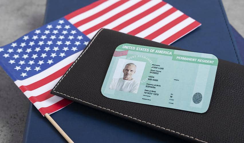 A U.S. permanent resident card placed on a passport next to an American flag, representing the EB5 path to lawful permanent residency in the United States.