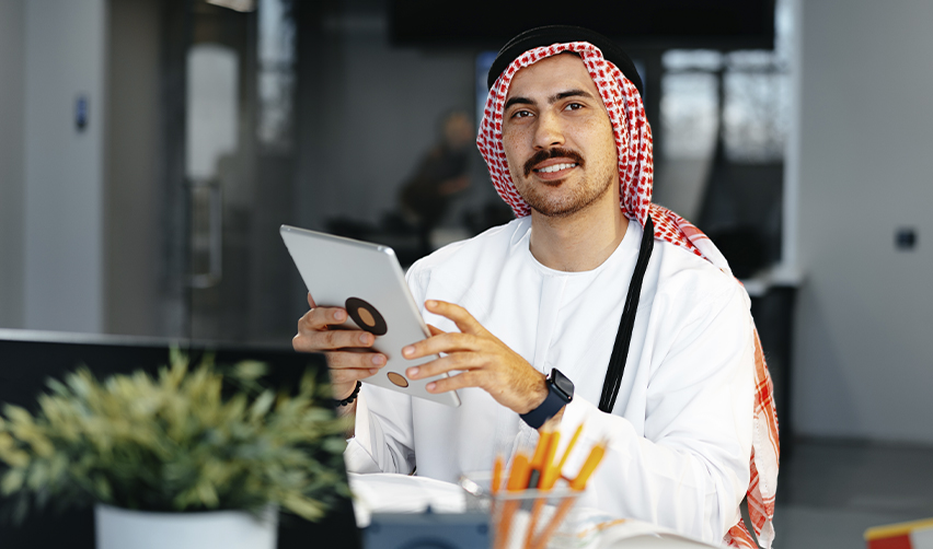 Middle Eastern businessman in traditional Gulf attire using a tablet in an office, representing Middle Eastern EB5 investors seeking fast U.S. green card options during regional instability.