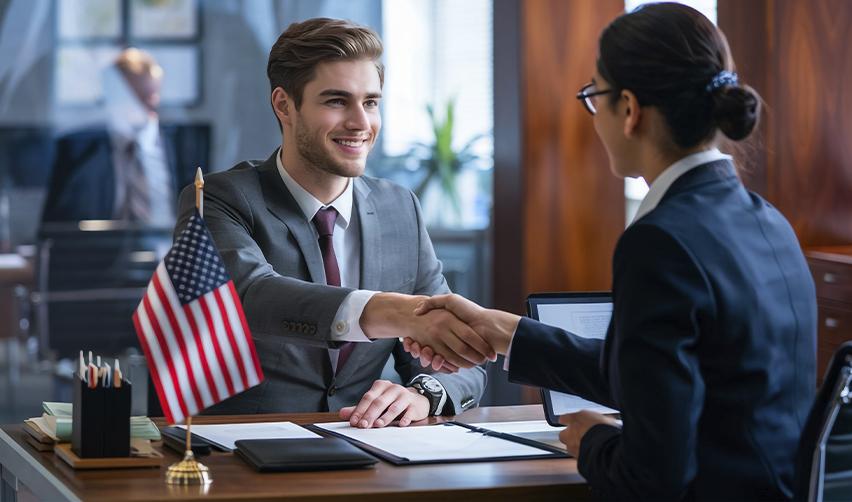 Investor shaking hands with advisor across a desk with US flag, representing EB5 investment decision and securing benefits under the RIA before the 2026 deadline.