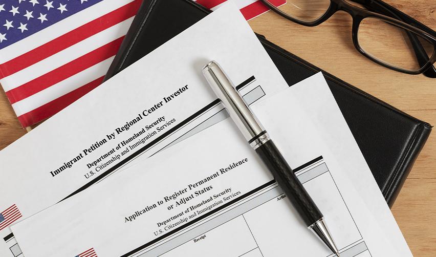 EB5 immigration forms and documents on a desk with US flag and pen, illustrating EB concurrent filing.
